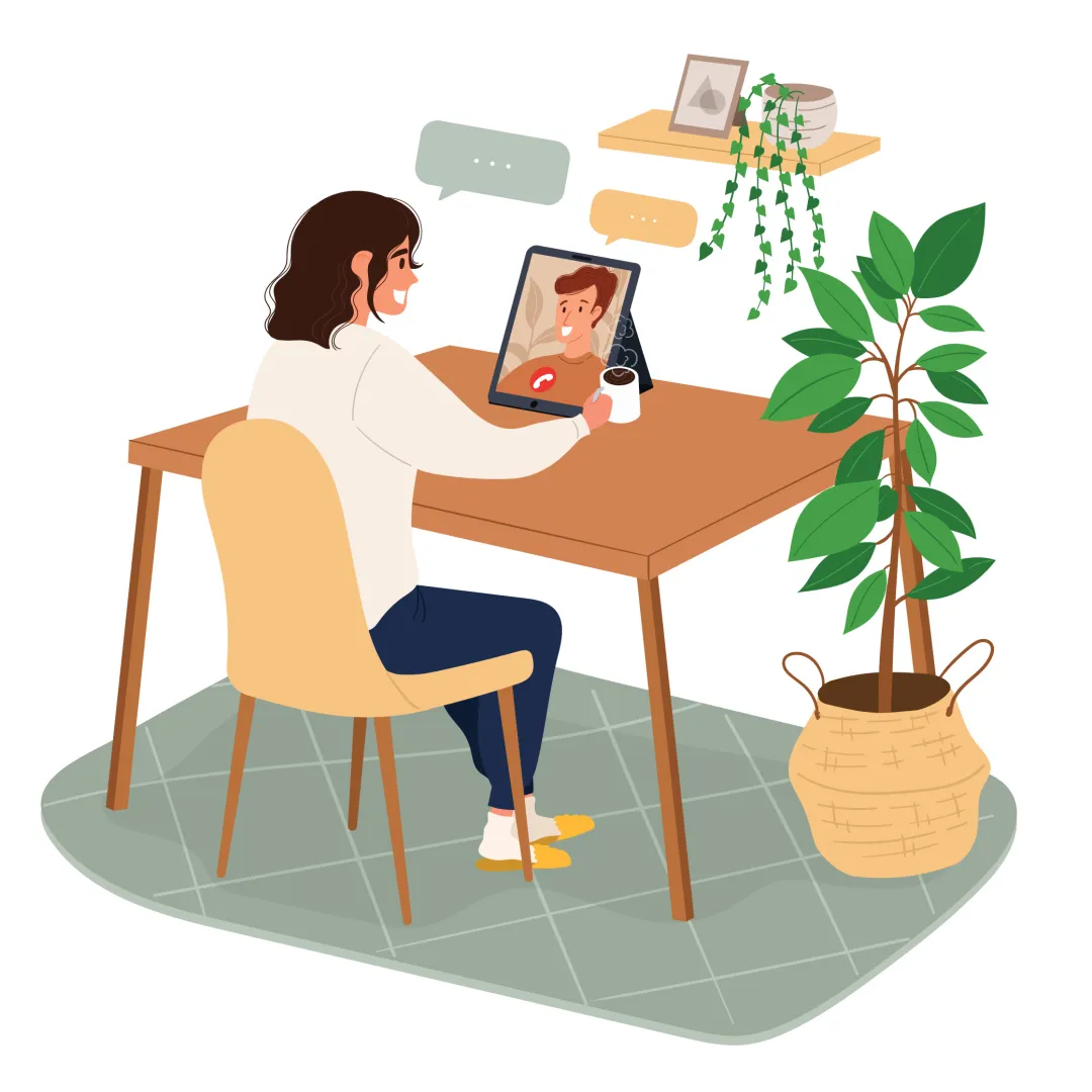 A woman seated at a table with a laptop and a plant nearby.