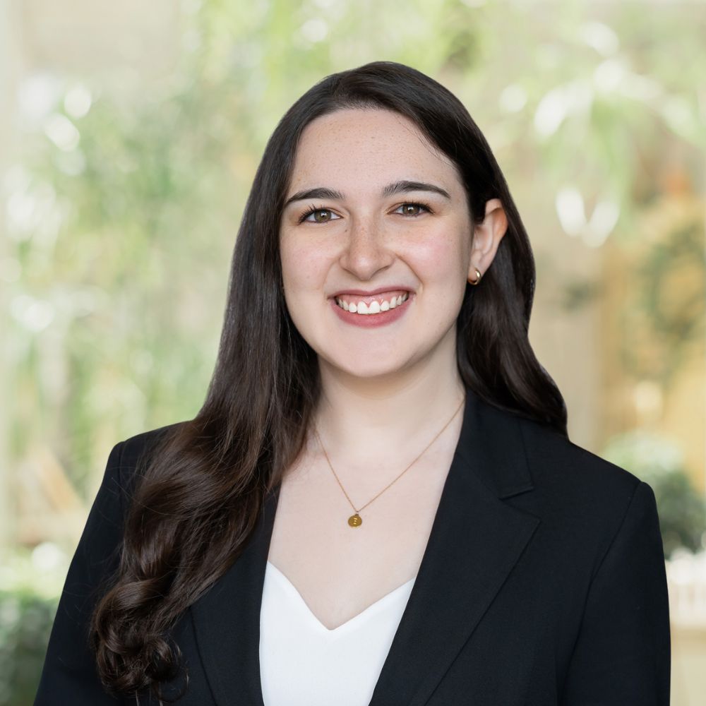 A professional woman wearing a suit, displaying a warm smile.