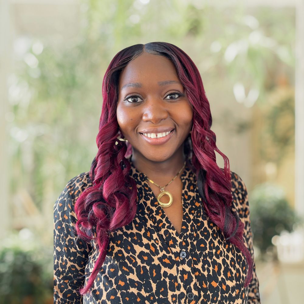 A woman with vibrant magenta hair wearing a stylish leopard print shirt.