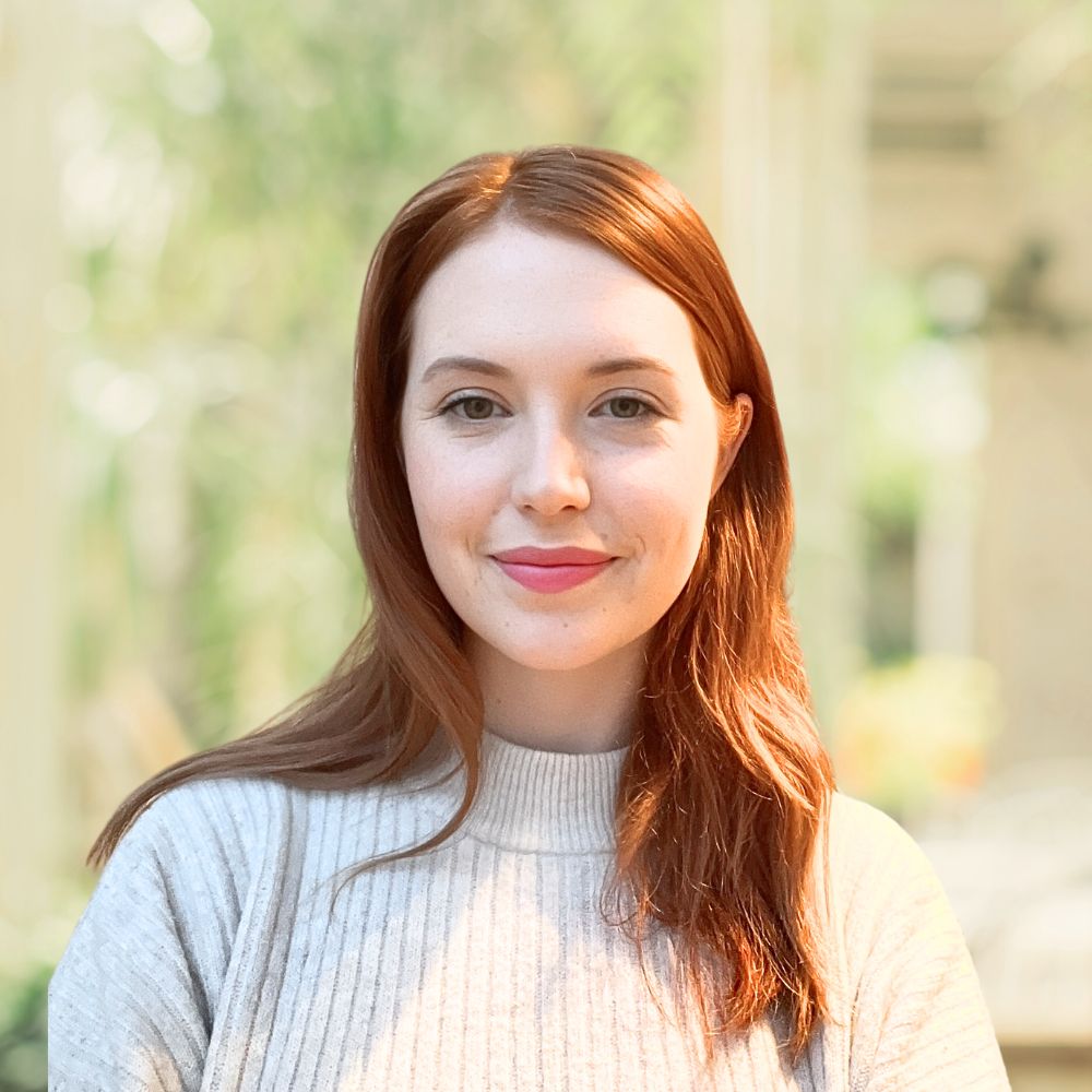 A woman with vibrant red hair wearing a cozy white sweater.