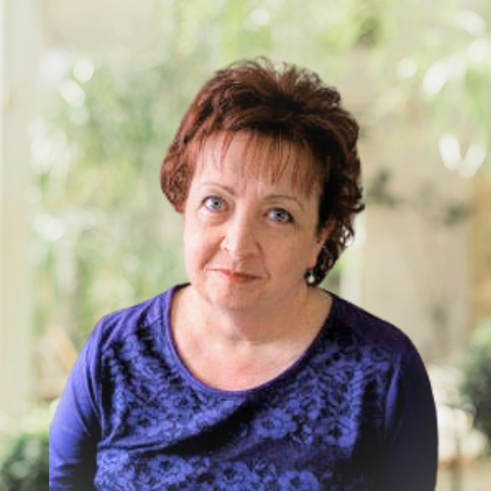 A woman with short hair wearing a floral purple shirt.