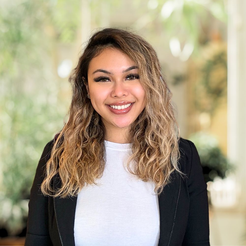 A smiling woman with wavy hair wearing a crisp white shirt.