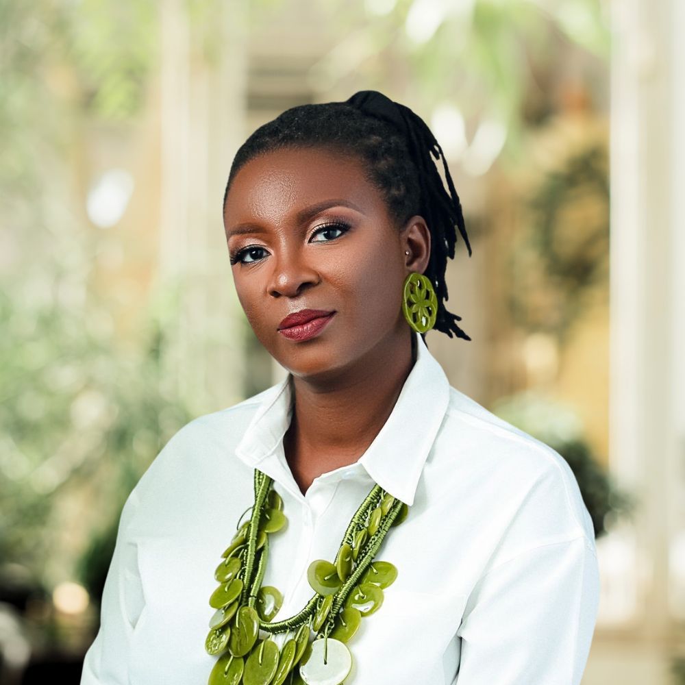 A woman with dreadlocks wearing a white shirt and green necklace exuding a unique sense of style and individuality.