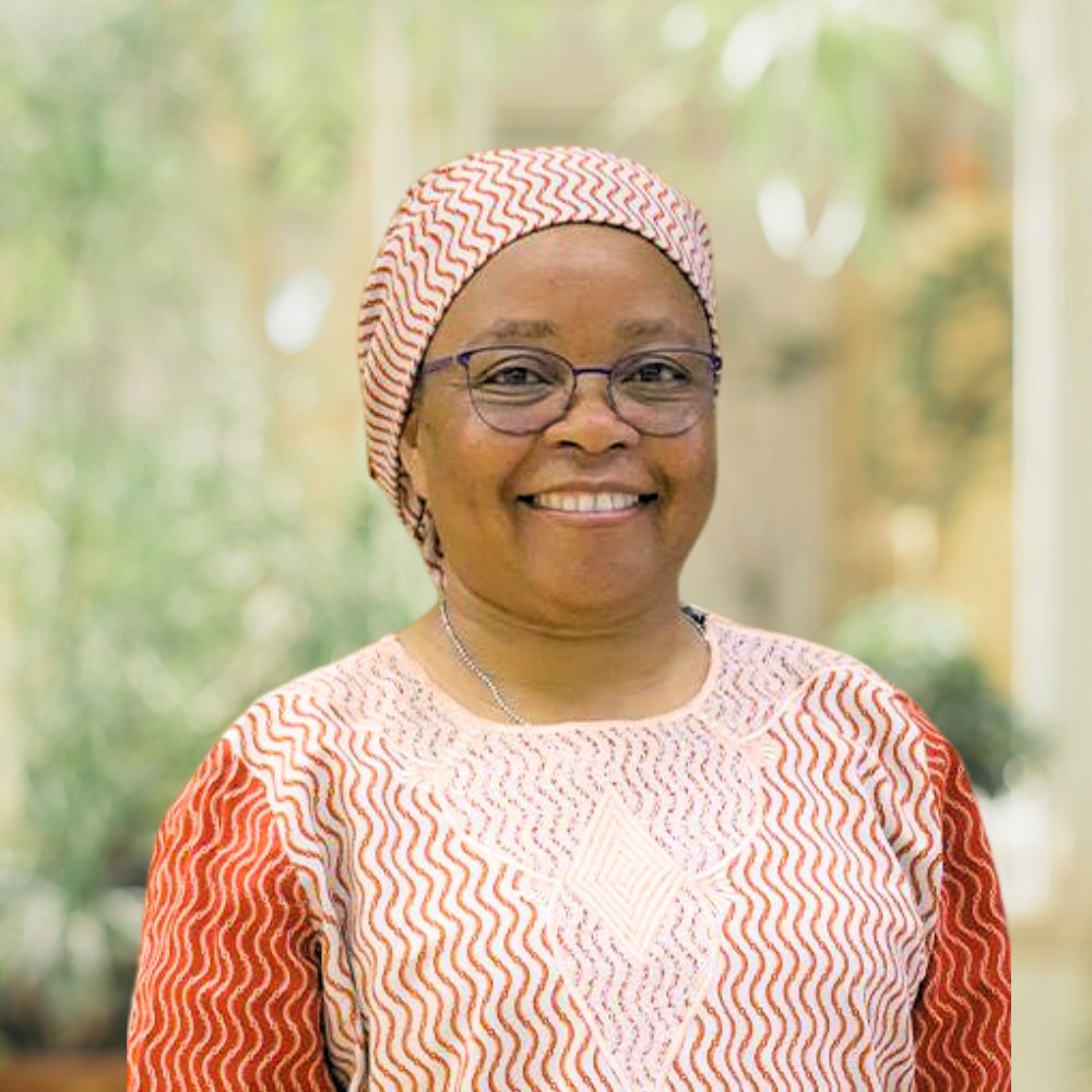 A smiling woman wearing glasses and a headscarf.