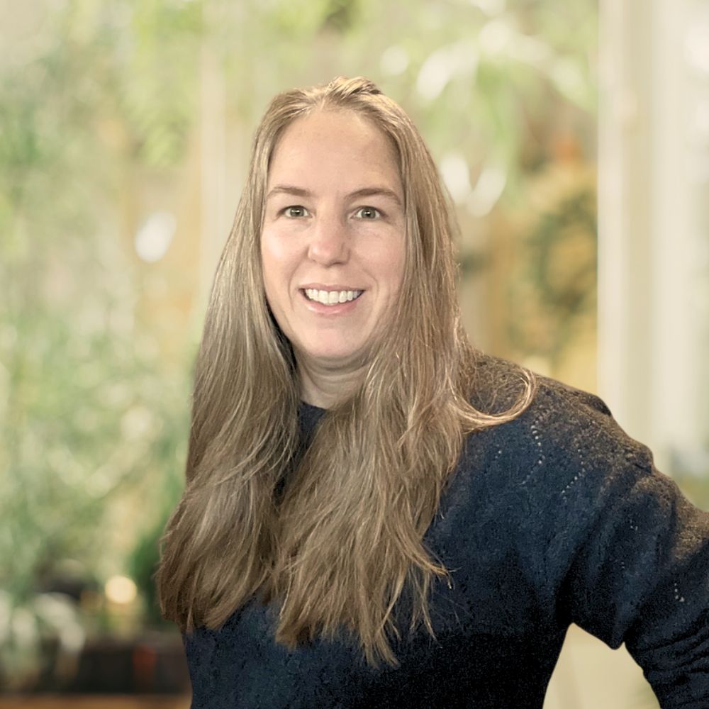 An elegant lady with flowing hair standing before a lush plant.