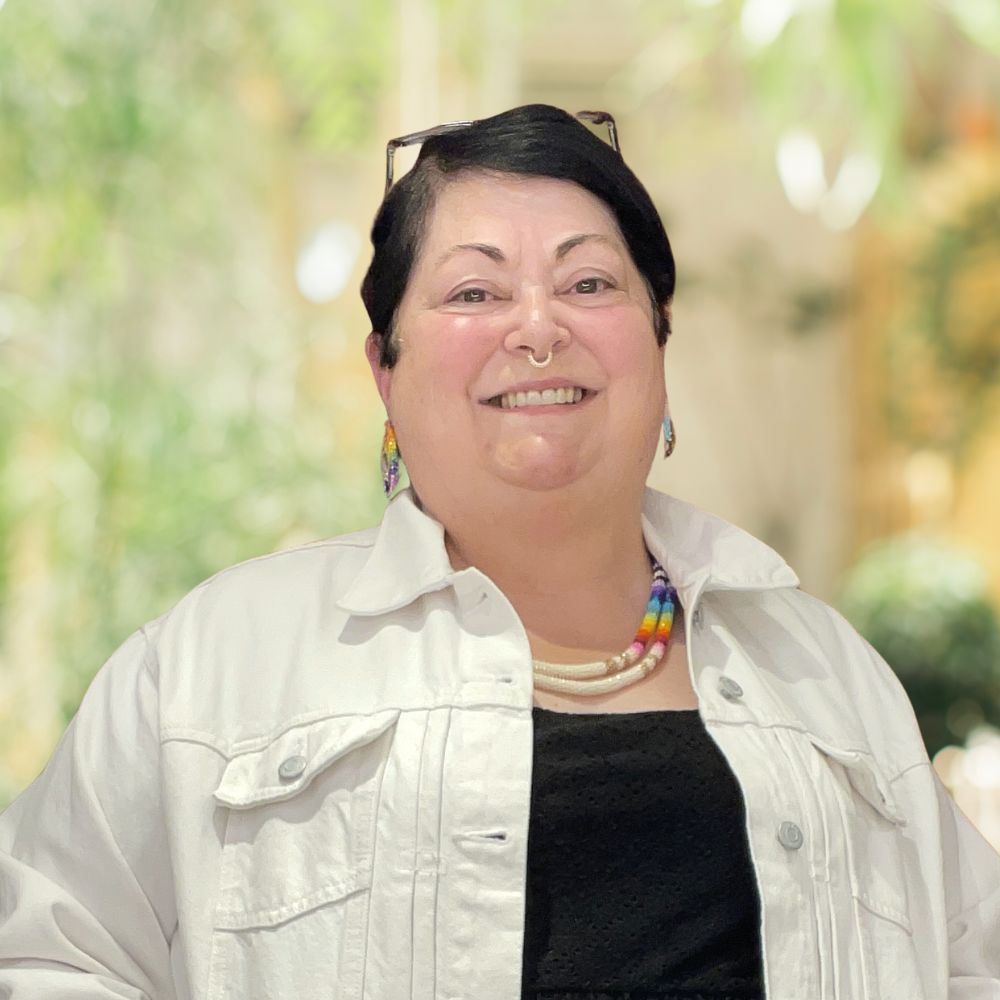 A woman in a black shirt and white jacket standing in front of a plant, exuding elegance and poise.