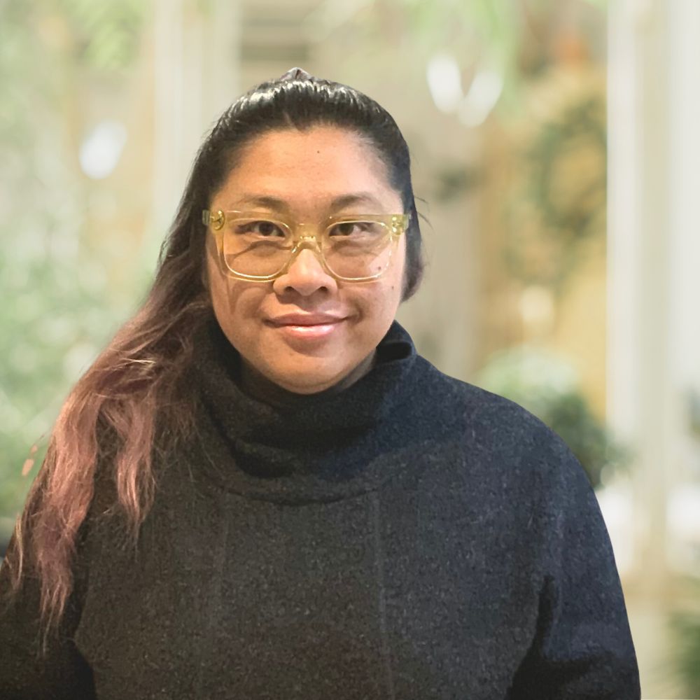 A smiling woman wearing glasses with a ponytail wearing a black sweater.