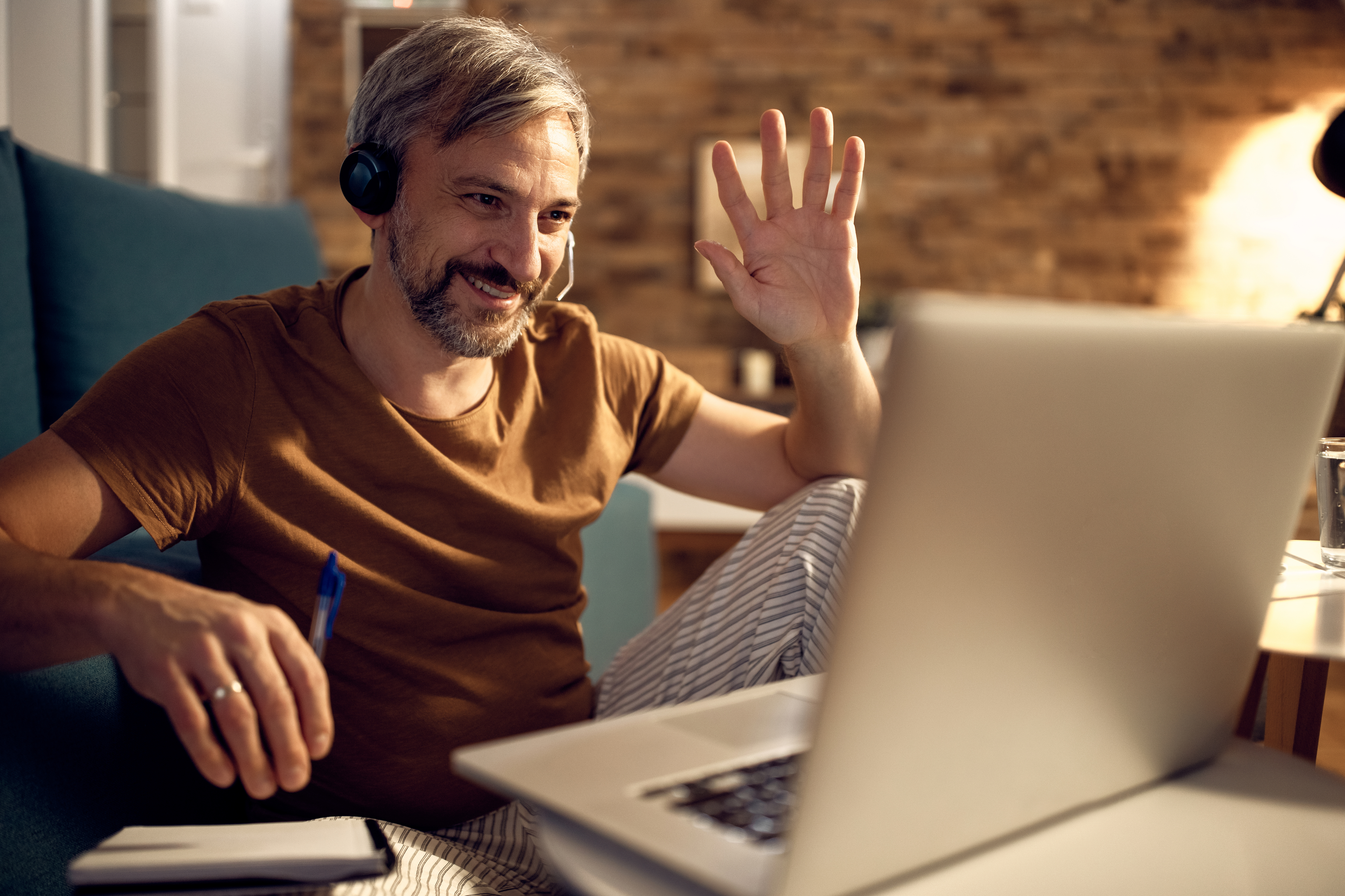 man waving at laptop screen while sitting on couch
